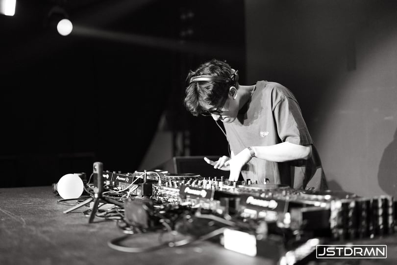 An EDM producer hunched over a mixing console, fine-tuning the core elements—leads, bass, and drums—while building loops, as discussed in 'Understanding the Core Components of an EDM Song.